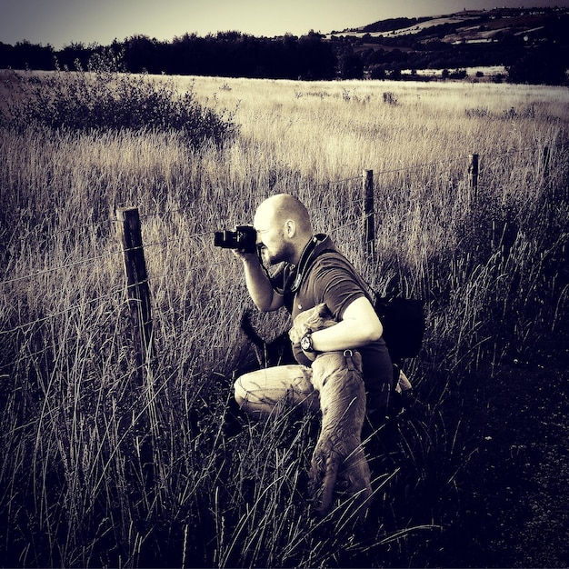 A photographer in the field capturing a stunning landscape shot, with a speech bubble pointing towards a laptop displaying stock photo website interfaces, illustrating the process of uploading and selling photos online.