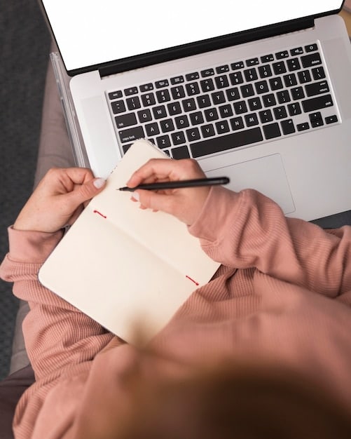 A close-up shot of a freelancer's hands typing on a laptop, with a notebook and pen nearby. The focus is on the hands and the laptop keyboard, suggesting daily financial tasks and bookkeeping.