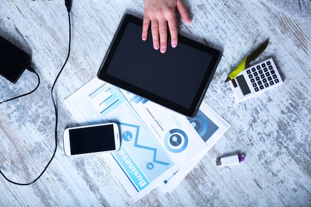 A person's hand pointing at financial charts and graphs on a laptop screen, with various financial documents and a calculator on the desk indicating financial analysis and planning.